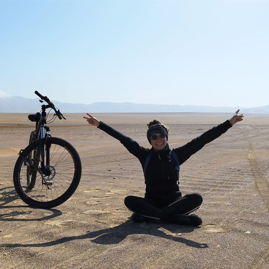Manon, cofondatrice de Dear Travel, bras levés à côté d’un vélo dans la réserve nationale de Paracas, au Pérou